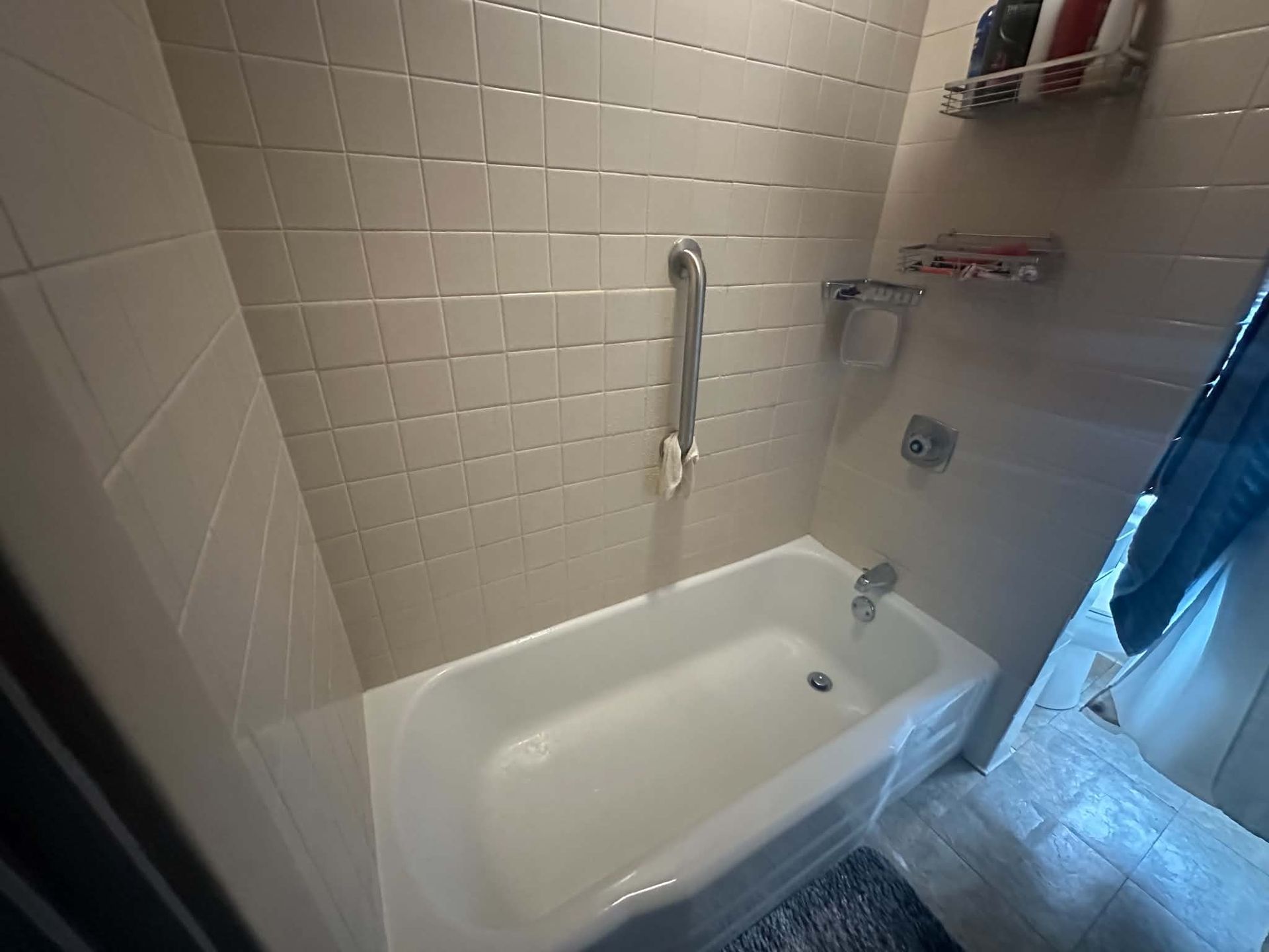 Small white bathtub with grab bar in a tiled bathroom near a shower curtain
