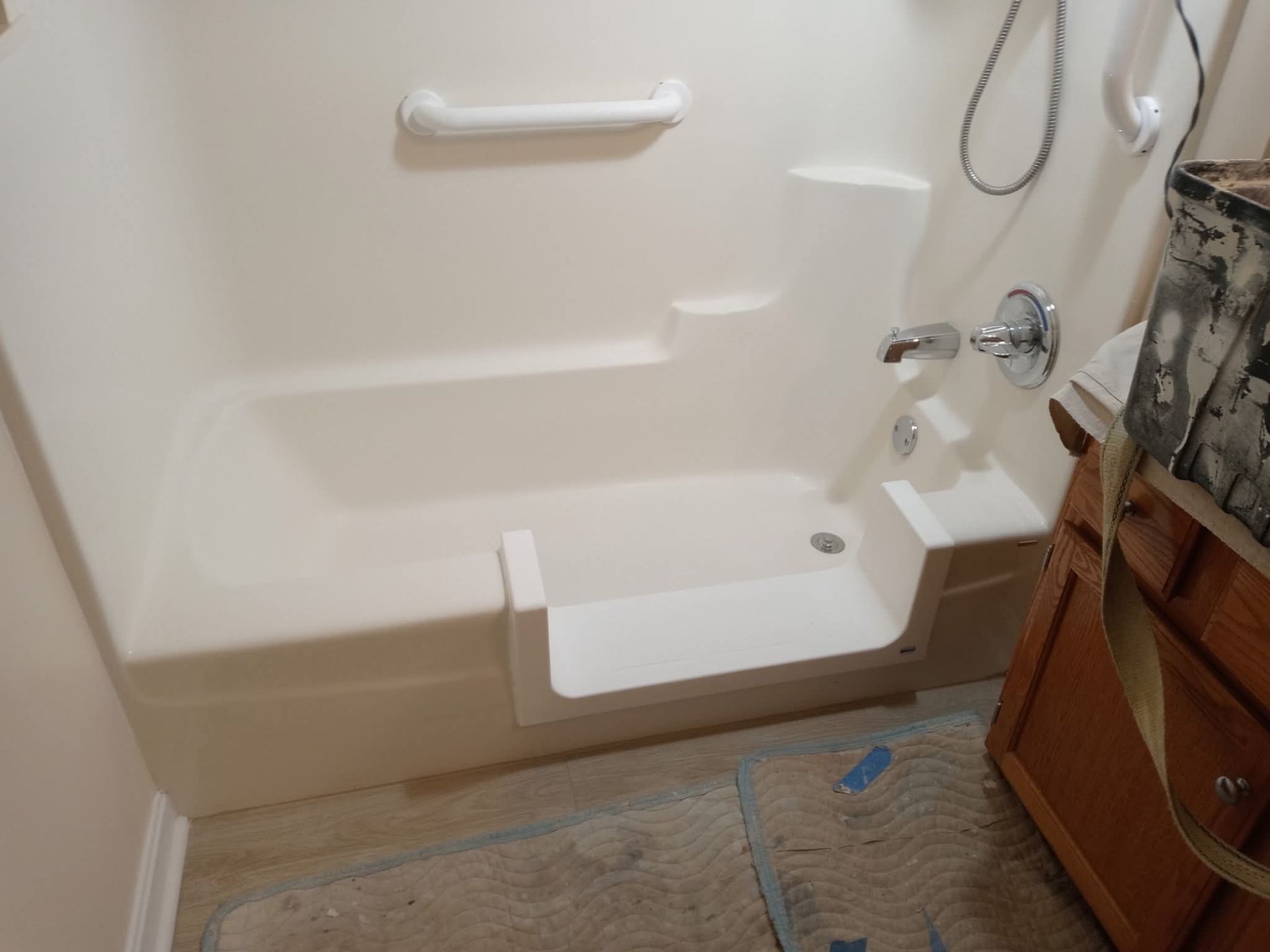 Accessible shower/tub with grab bars, fold-down seat, and handheld showerhead in a bathroom.