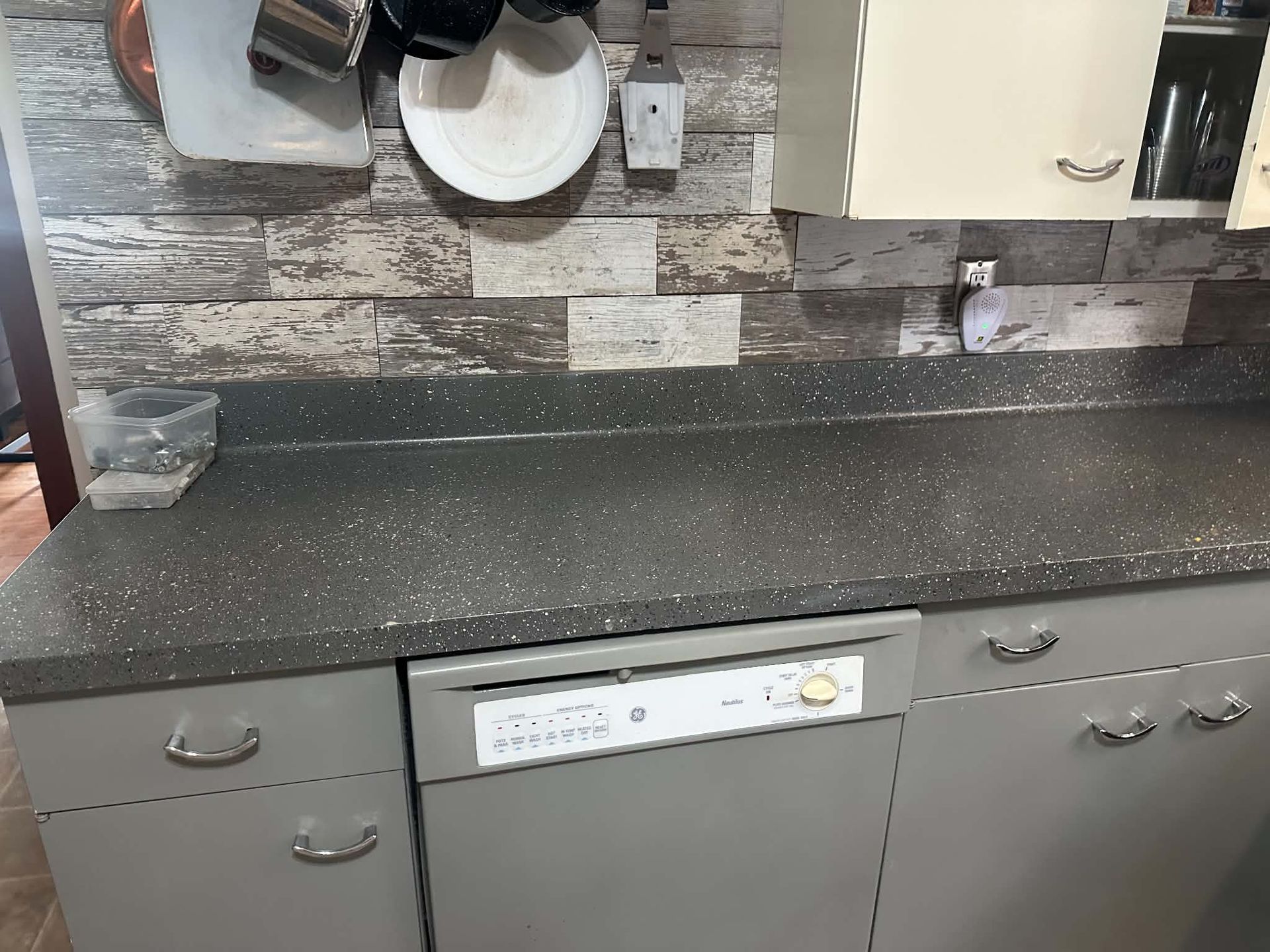 Kitchen countertop with gray cabinets, speckled dark surface, and a built-in dishwasher.