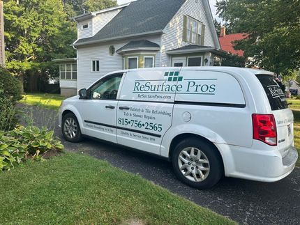 White van with “ReSurface Pros” branding parked in a driveway beside a house and lawn