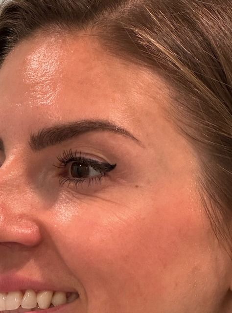 Woman's smiling face in profile, with dark eyeliner and visible fine lines near the eye.