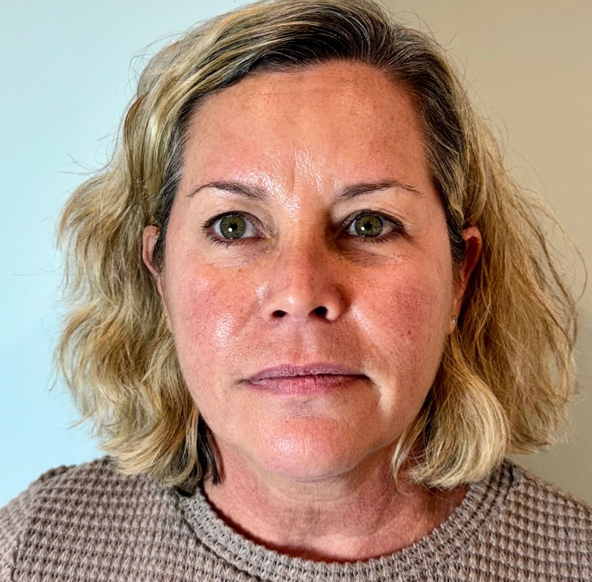 Woman with short blonde hair, wearing a brown sweater, looking directly at the camera.