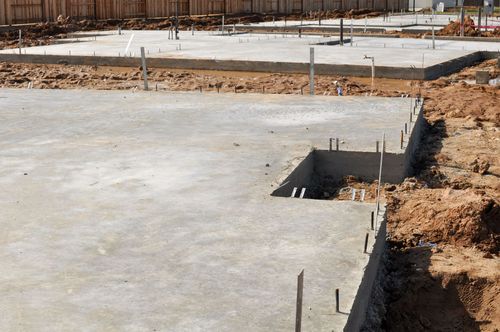 Concrete foundation slab at a construction site with exposed rebar and dirt trenches around the edges