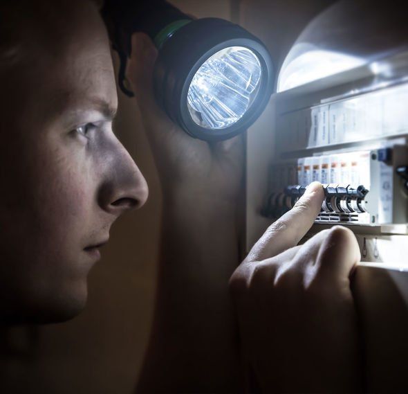 Man using a flashlight to examine a fuse box, looking concerned.
