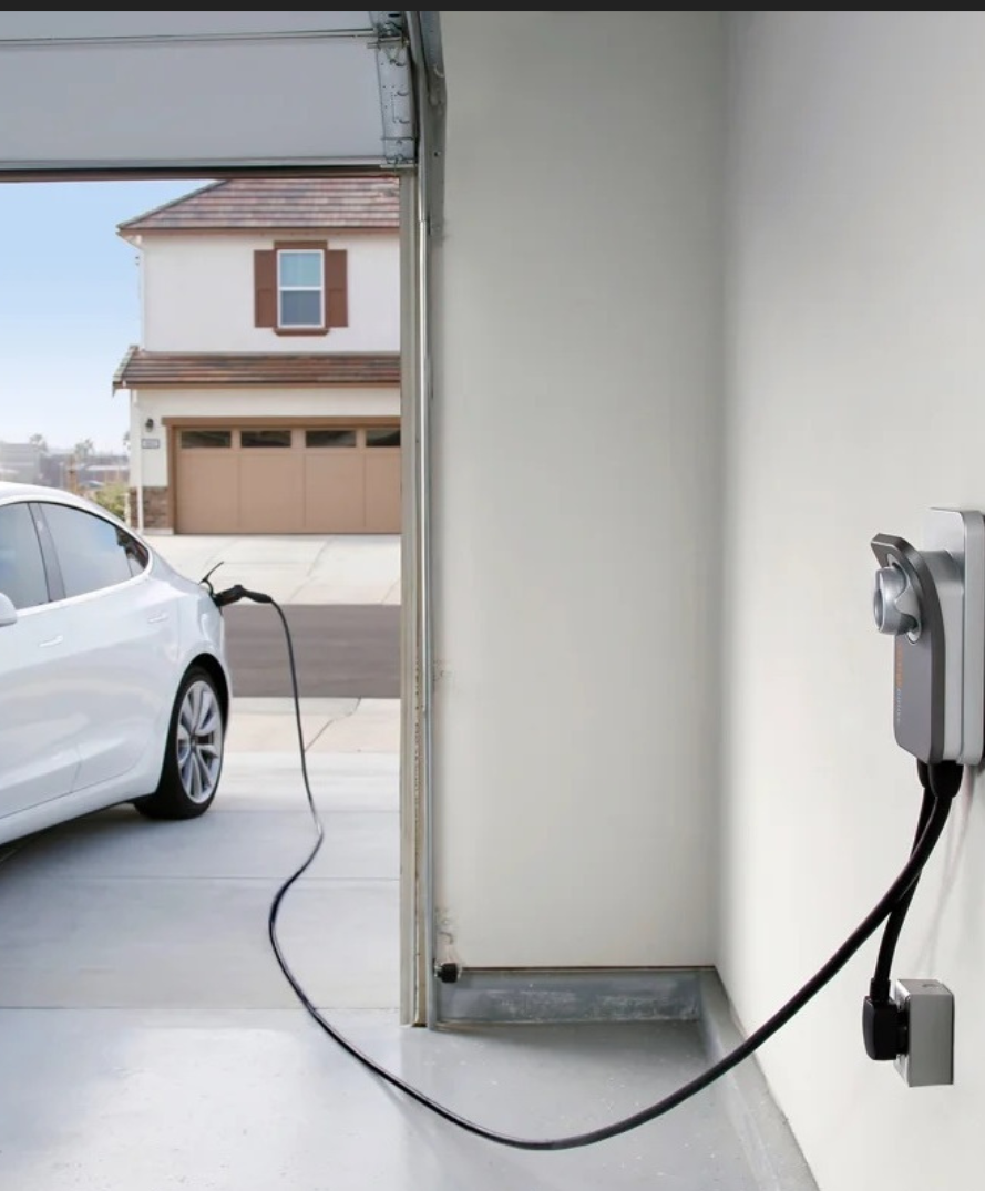 White electric car charging in a garage with charger mounted on the wall.