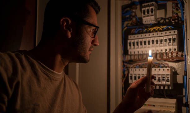 Man holding a lit candle, inspecting a fuse box in the dark.