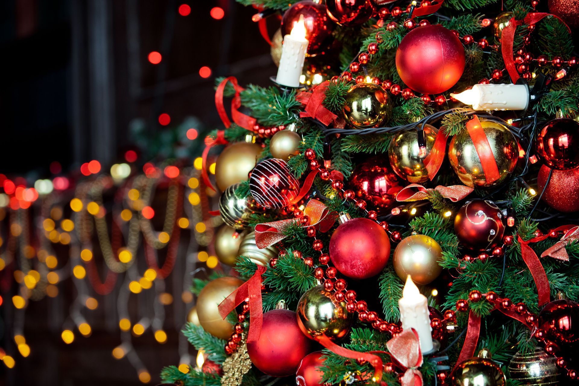 Christmas tree with red and gold ornaments, lights, and candles.