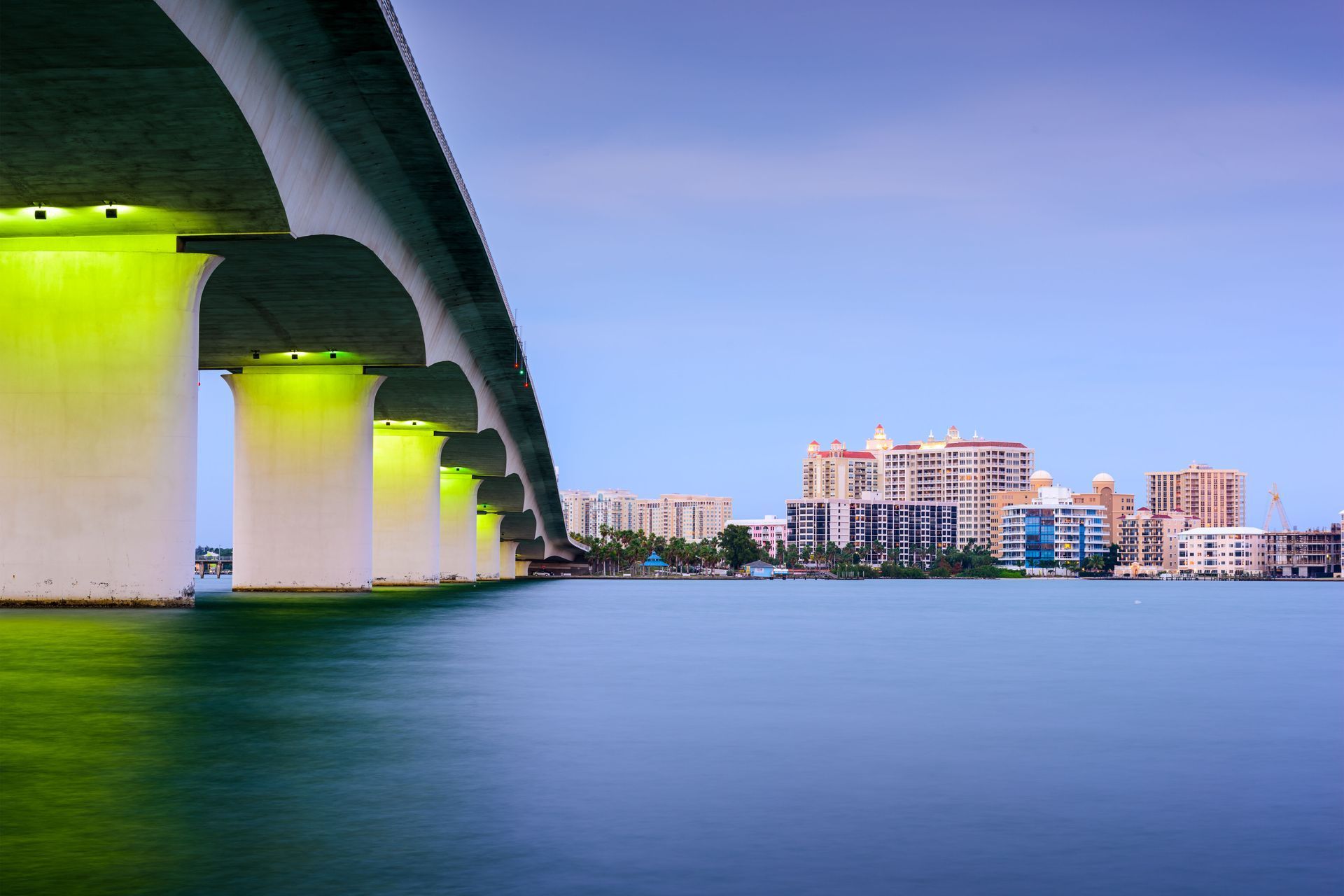 Bridge over water with buildings in the distance; the underside of bridge is lit green.