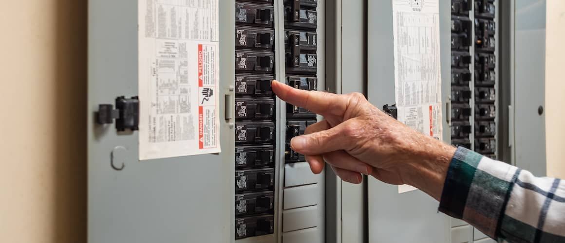 Person's hand reaching for a circuit breaker on a gray electrical panel.