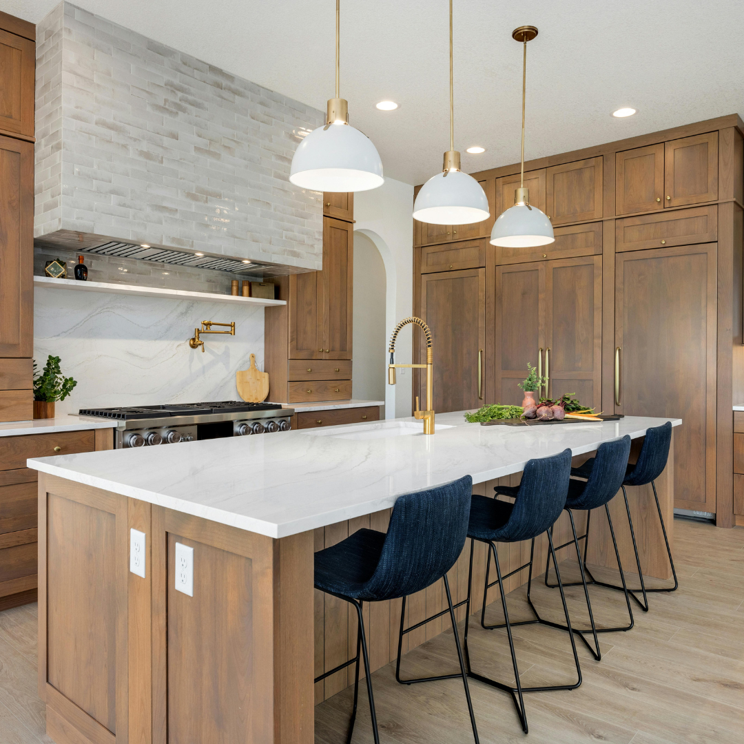 Modern kitchen with wood cabinets, white island, blue bar stools, and pendant lights.