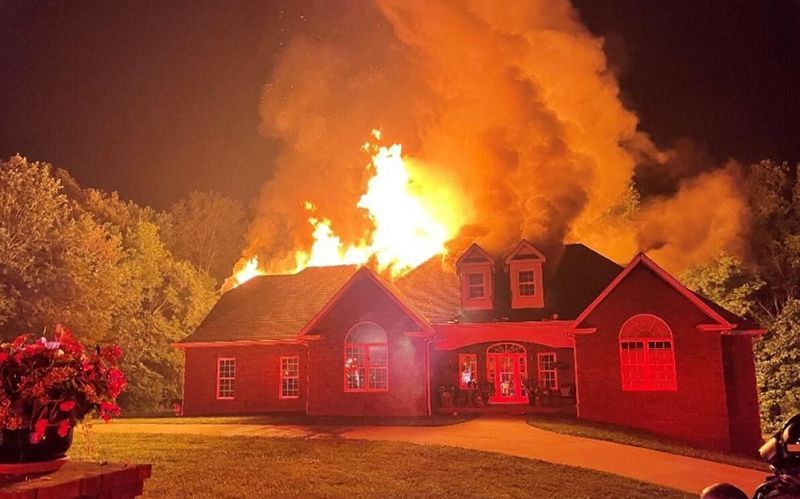 House engulfed in flames at night; intense orange fire against dark sky.