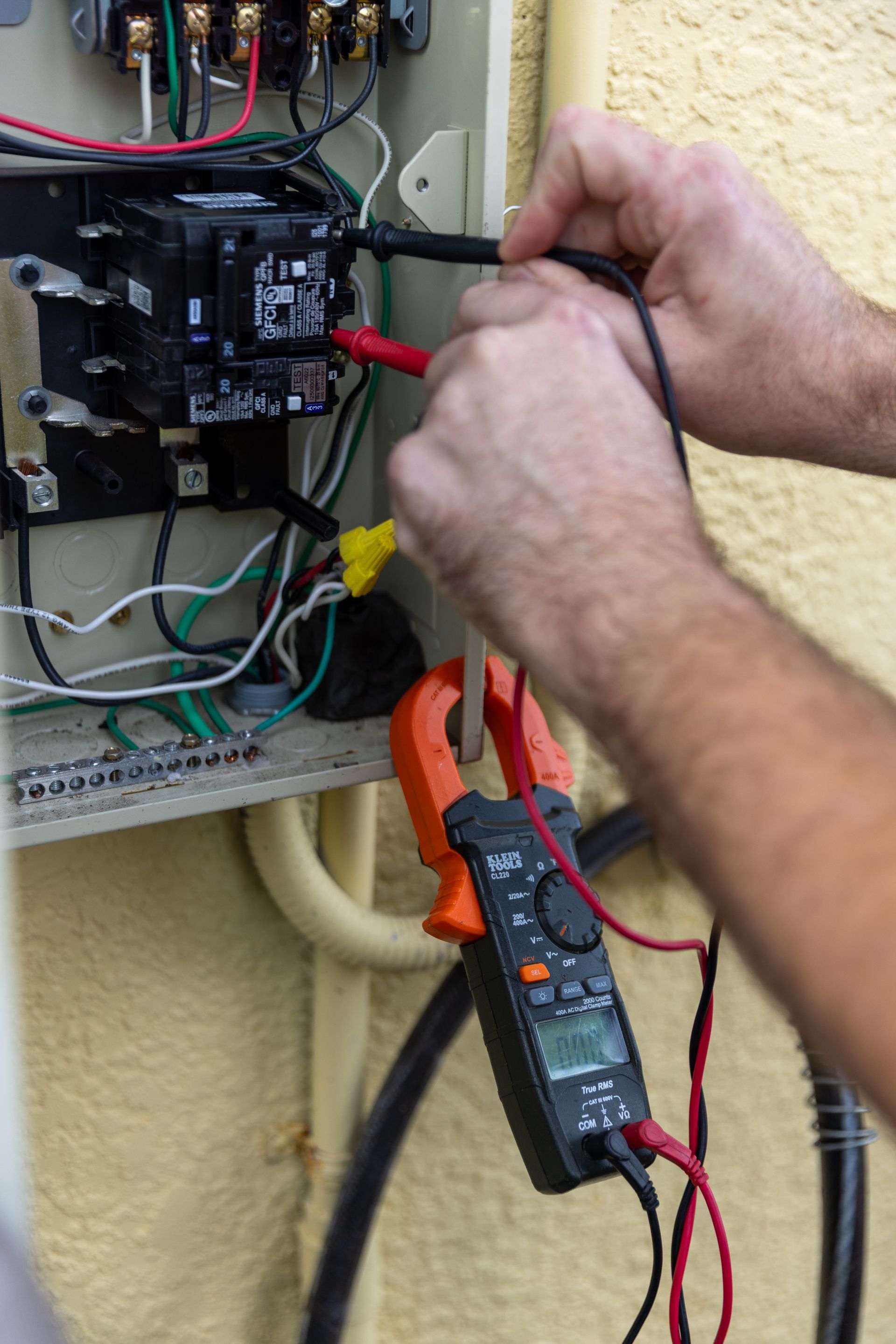 Hands using a multimeter to test electrical connections in an outdoor panel.