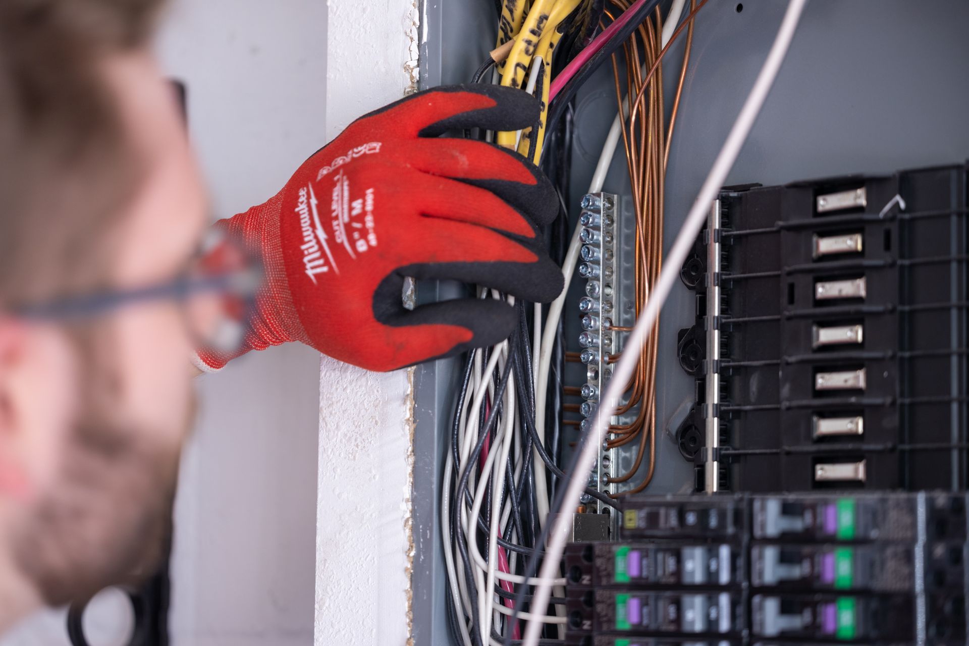 Person in red gloves working on electrical wiring in a panel.