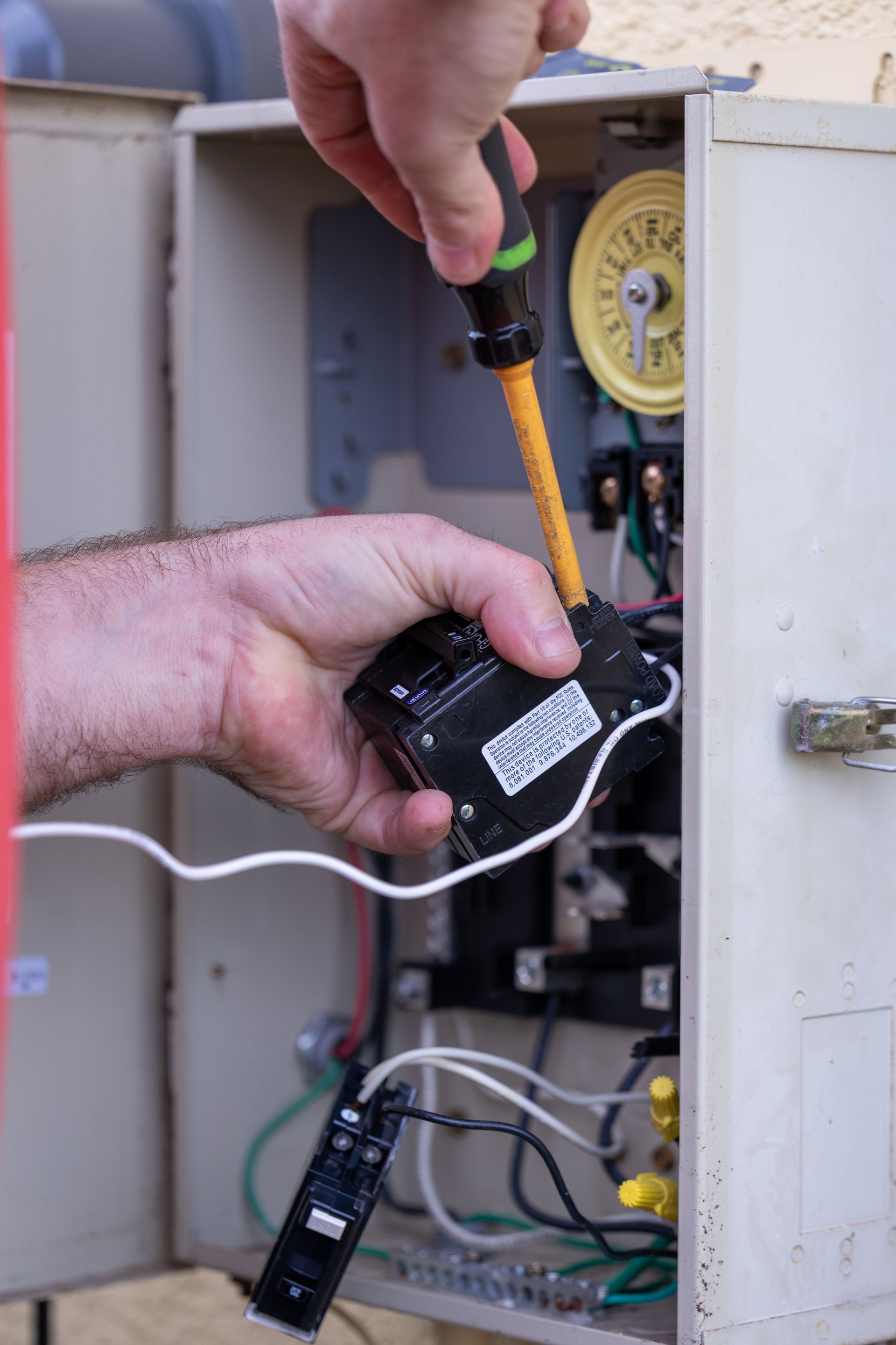 A person using a screwdriver to work on electrical components inside a metal box.