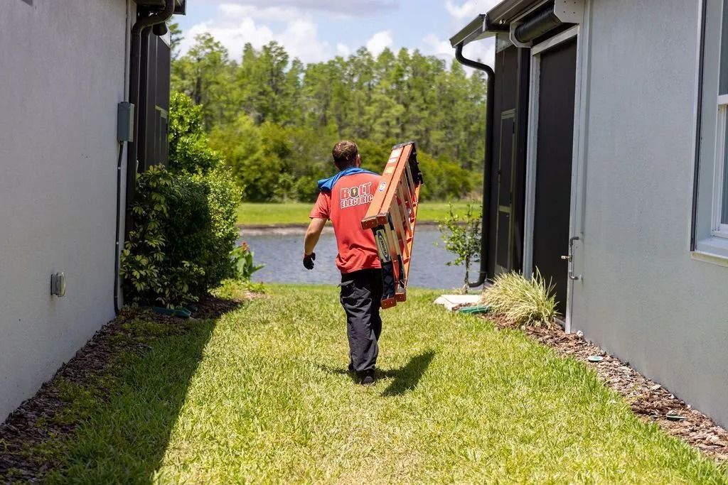 A person carries a large item down a grassy path between two houses towards a lake.