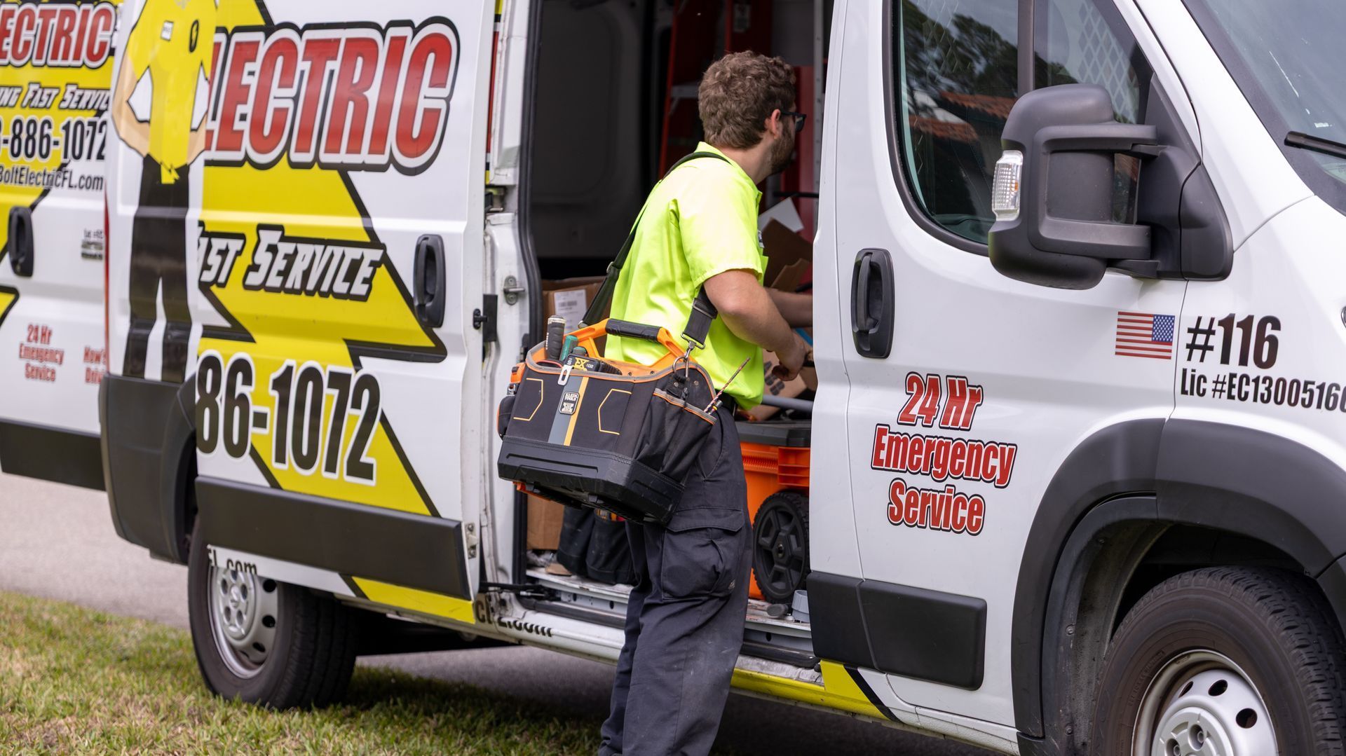 Electrician exits service van, carrying a toolbox. Van has company logo and phone number.