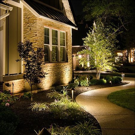 Night view of a house with stone siding illuminated by landscape lighting.