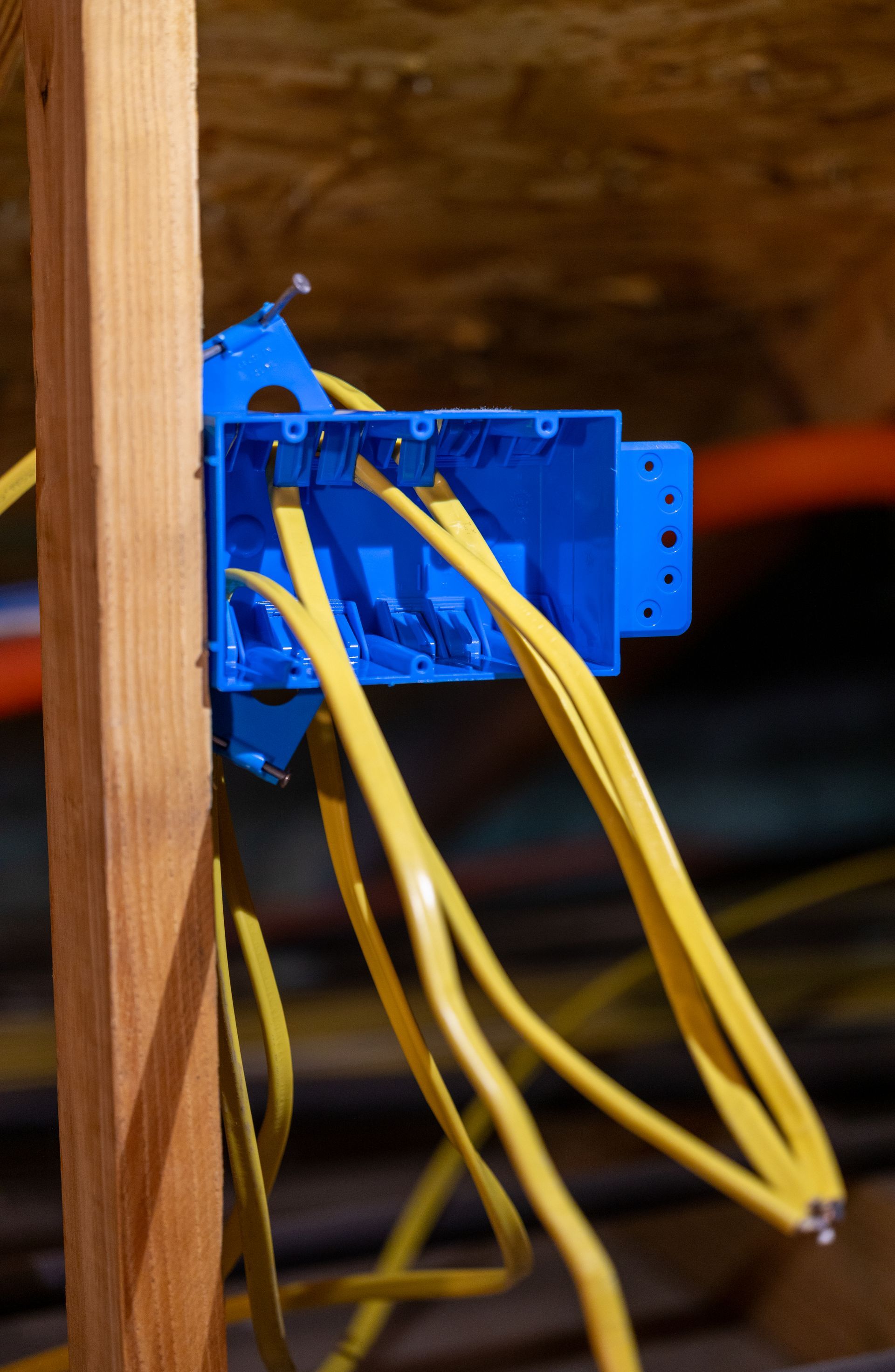 Blue electrical box on a wood stud with yellow wires extending.