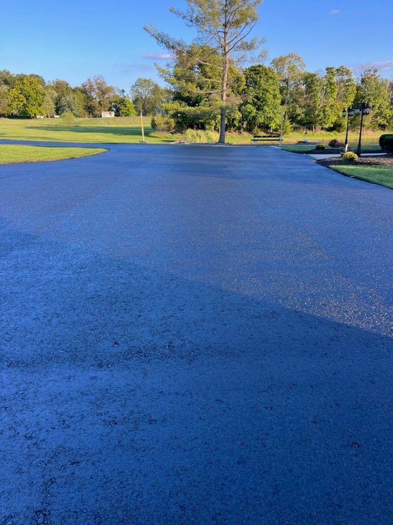 a black asphalt driveway leading to a golf course with trees in the background .