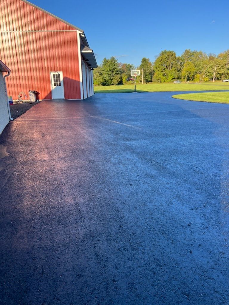 a black asphalt driveway with a red barn in the background