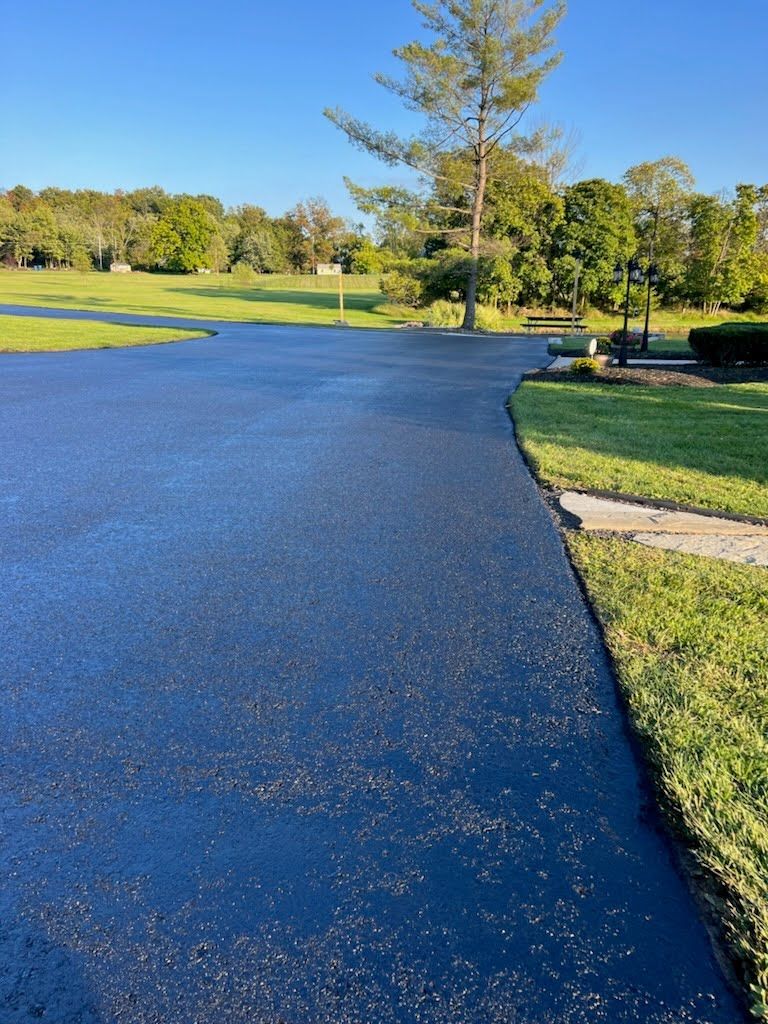 a asphalt driveway leading to a golf course with trees in the background .
