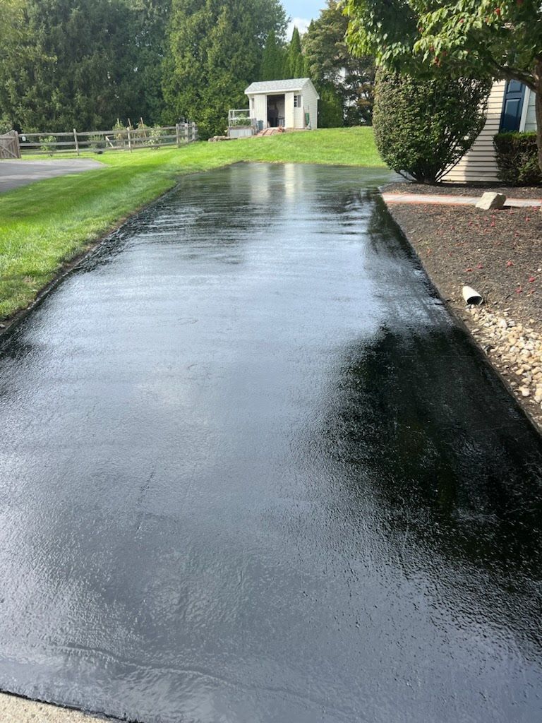a black asphalt driveway with a white house in the background .