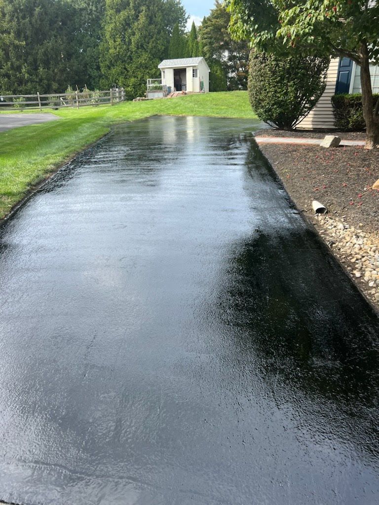 a black asphalt driveway with a house in the background .