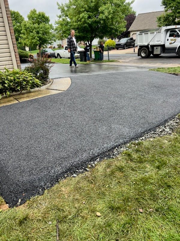 a man is walking down a newly paved driveway next to a dump truck .