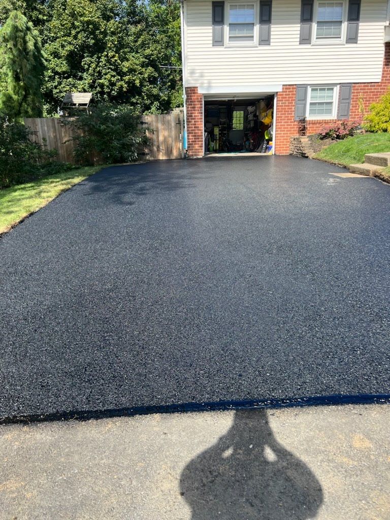 a shadow of a person is cast on a newly paved driveway in front of a house .