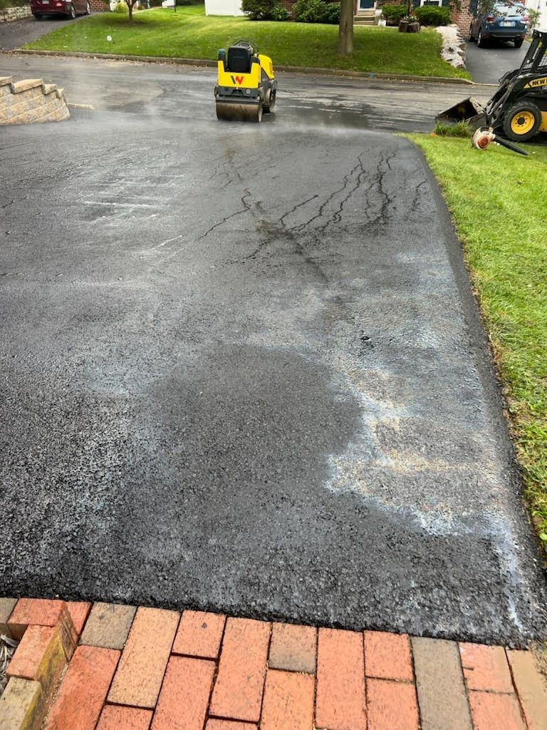 a yellow roller is rolling asphalt in a driveway .