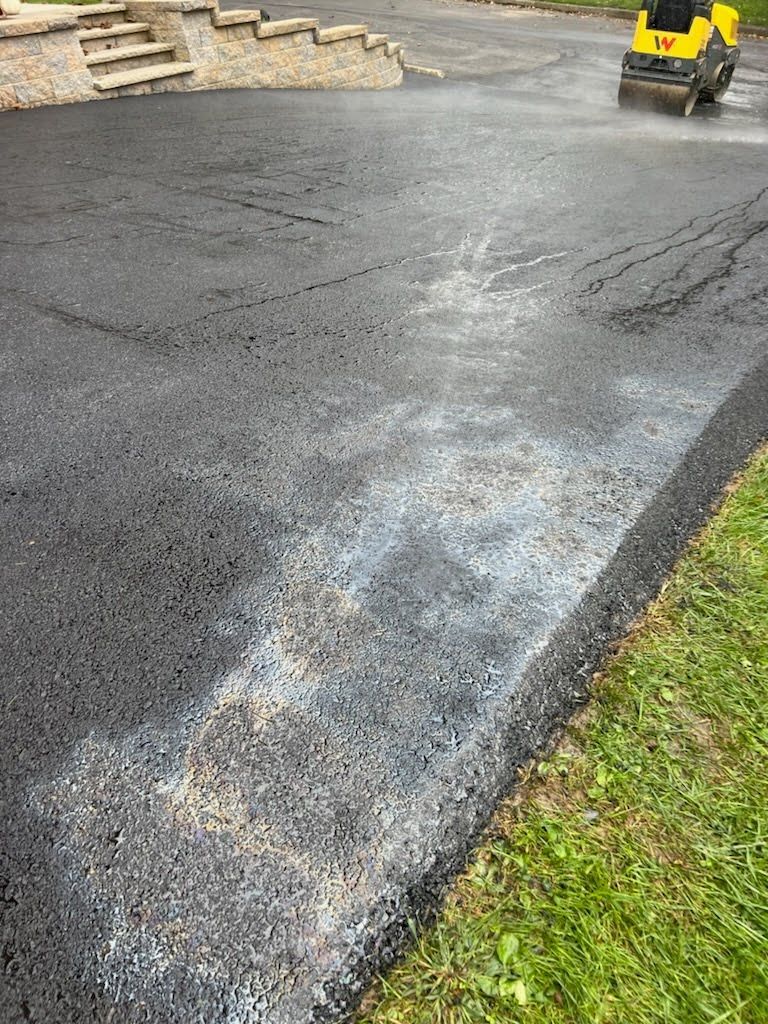 a yellow roller is rolling asphalt in a driveway .