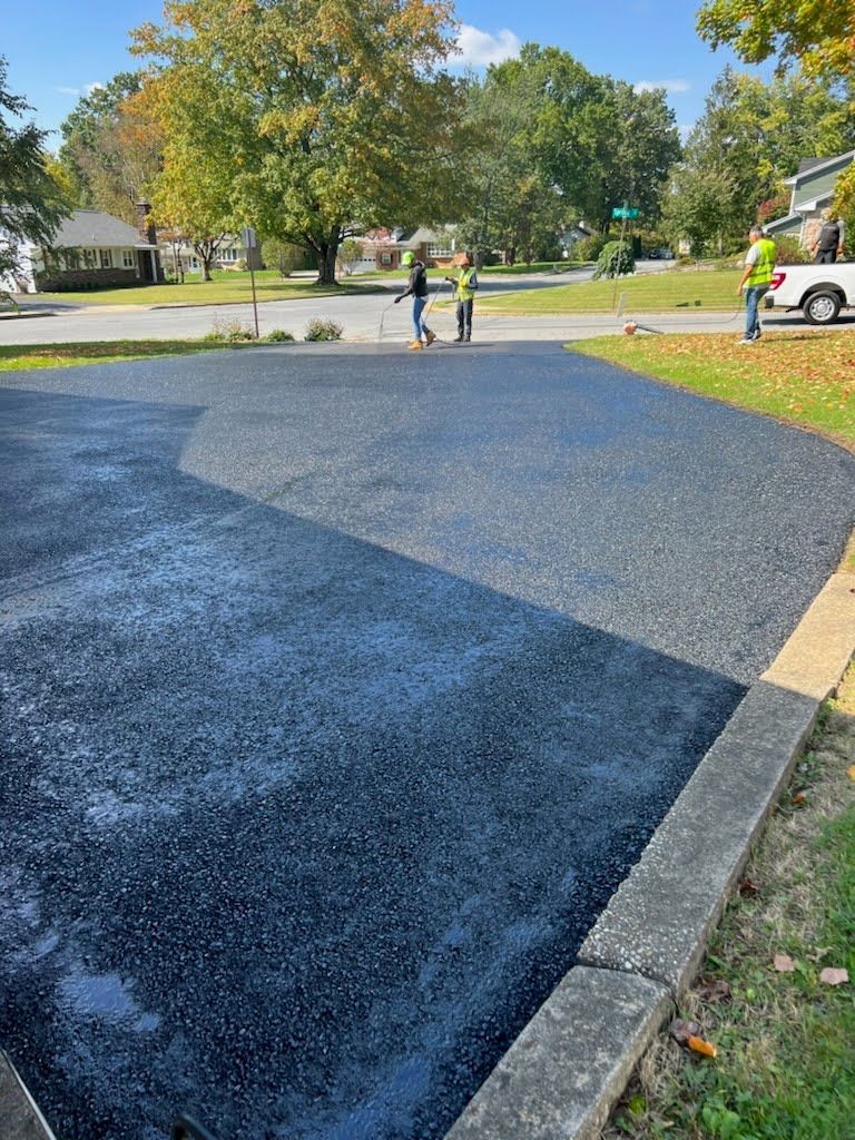 a couple of people standing on top of a black asphalt driveway .