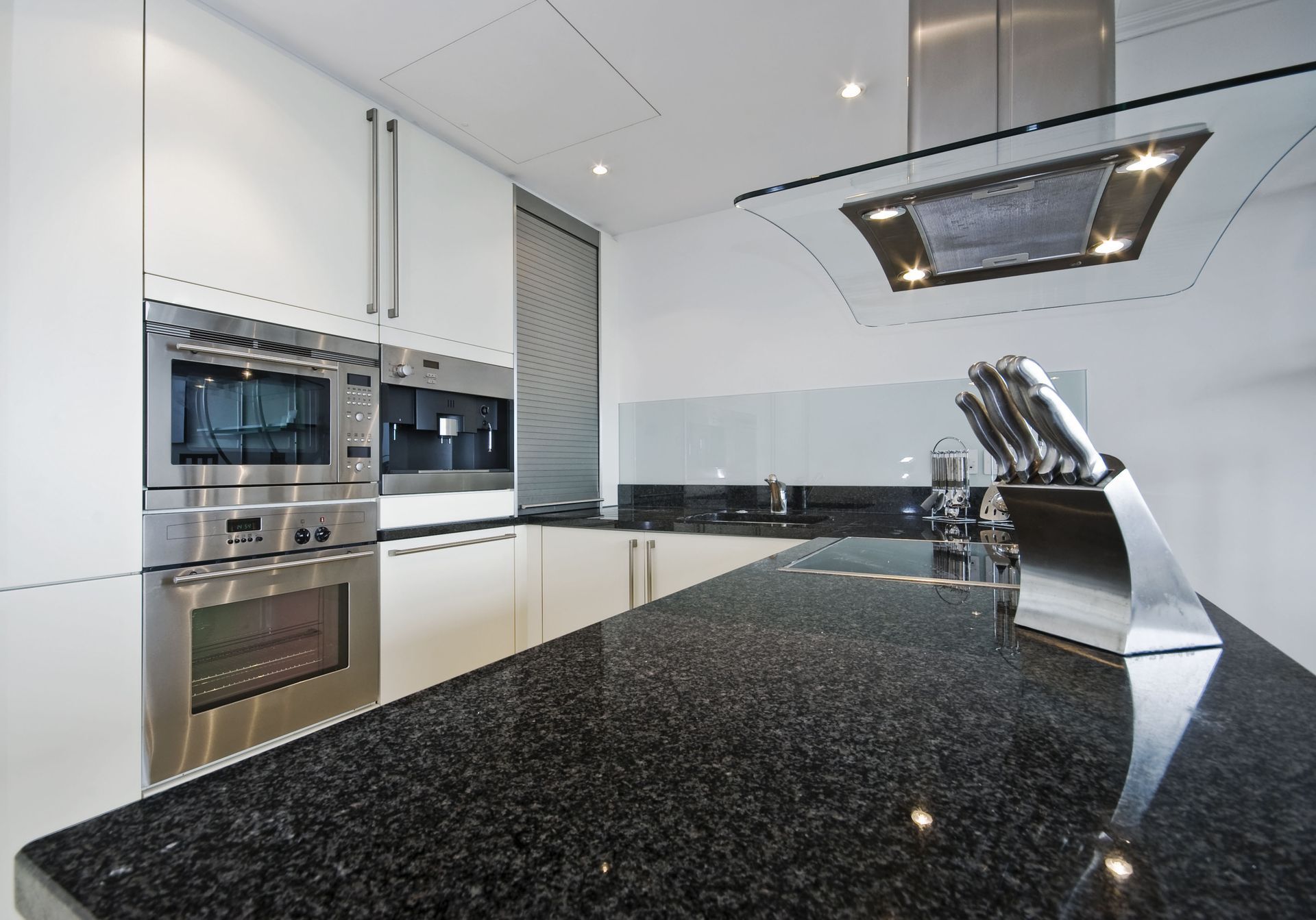 Modern kitchen with black granite countertop, stainless steel appliances, and white cabinets.