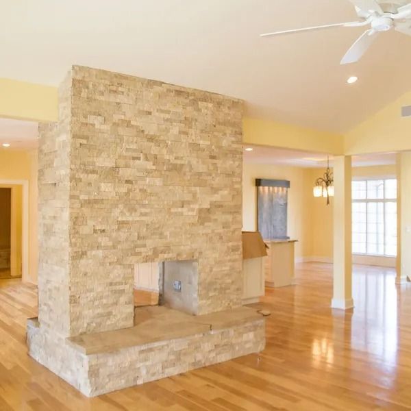 Stone fireplace in a room with hardwood floors and yellow walls; ceiling fan overhead.