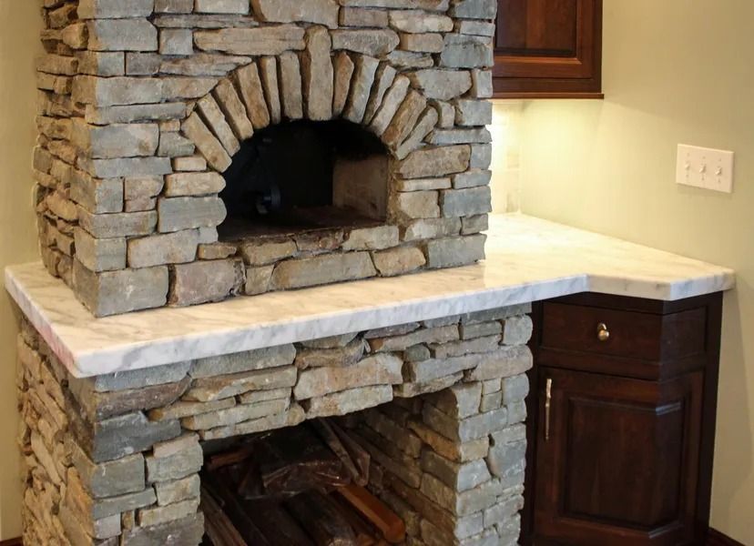 Stone pizza oven built into countertop with arched opening and wood storage.