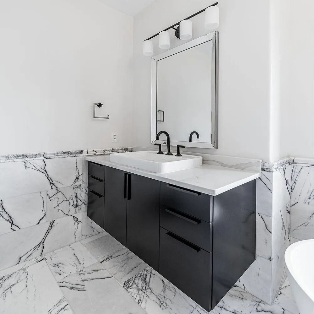 Modern bathroom with black vanity, white countertop, marble tile, and large mirror.