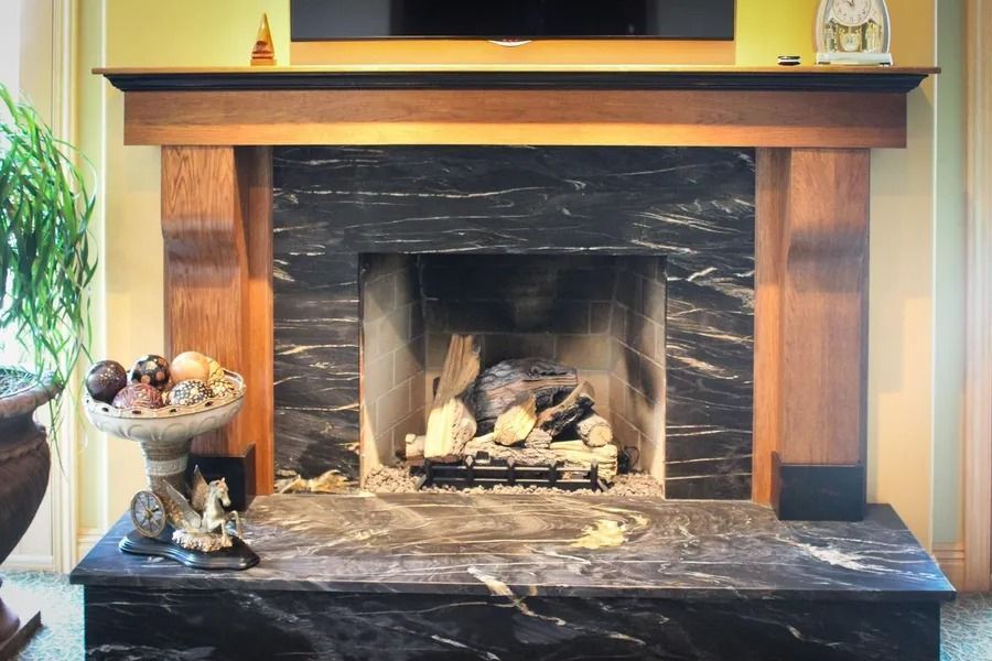 Fireplace with black marble surround, wood mantel, and hearth; logs inside.