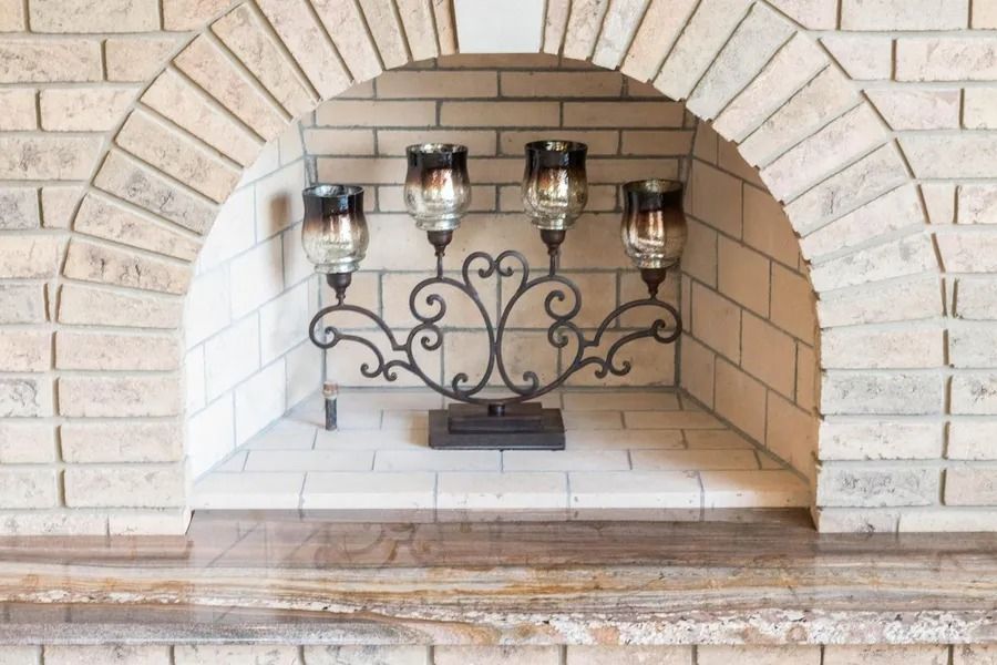 Candelabra with four lit candles inside an arched brick fireplace alcove.