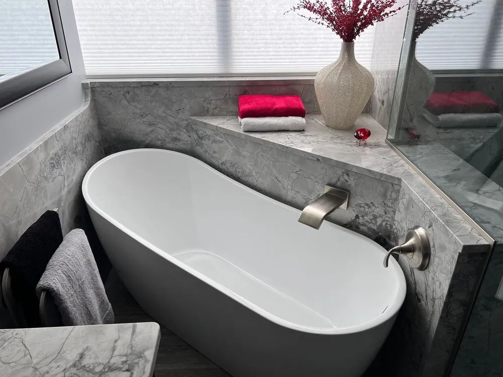 Modern bathroom with a white oval bathtub, gray stone accents, and decorative vase.