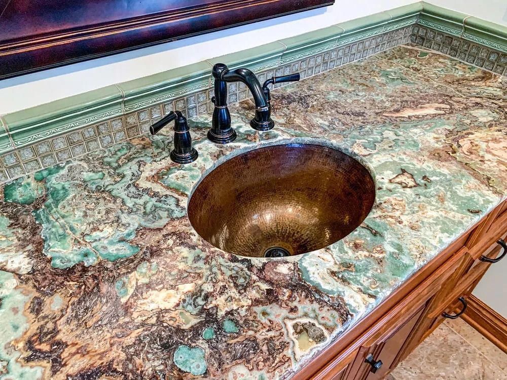 Bathroom vanity with copper sink, dark faucet, and green and brown patterned countertop.