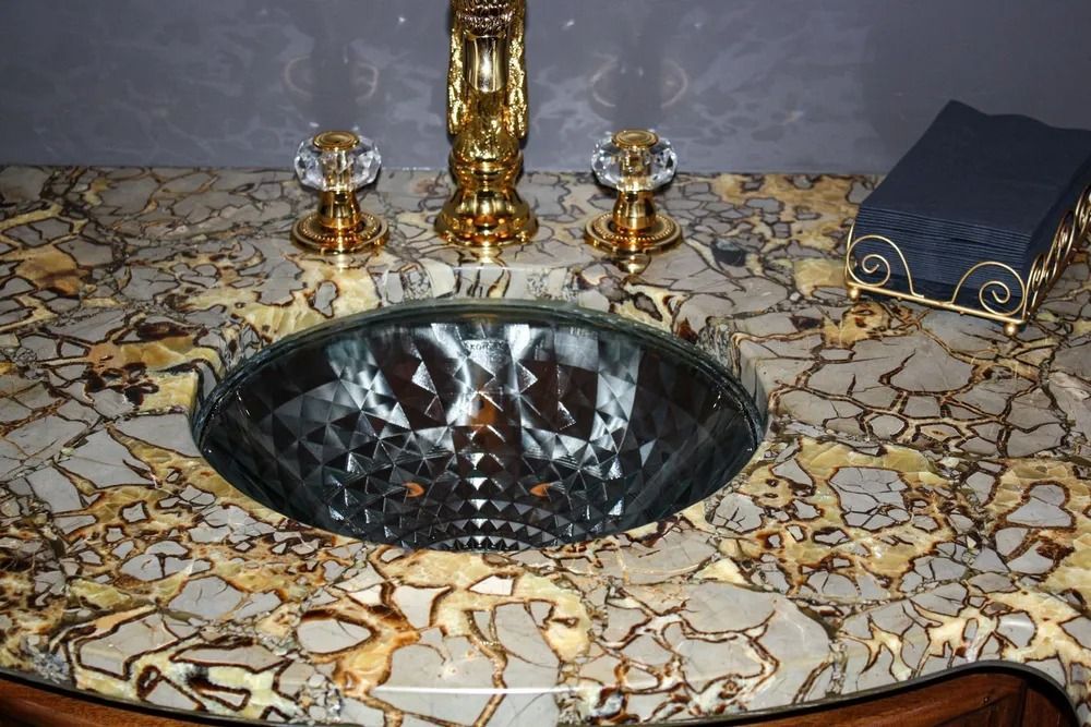 Bathroom sink with gold fixtures, a faceted glass bowl, and patterned countertop.