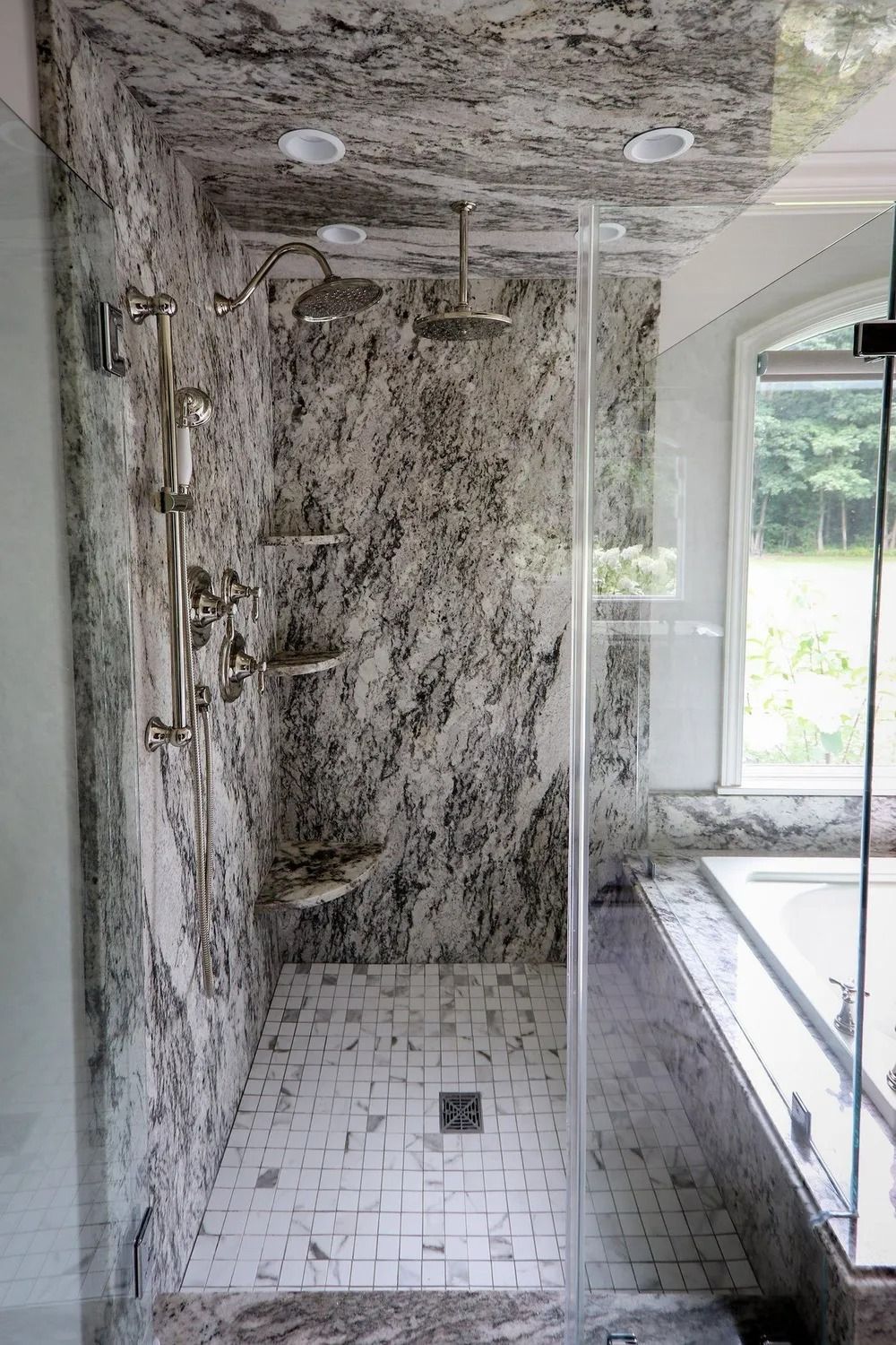 Elegant marble shower with glass doors and built-in shelves; a window is visible in the background.