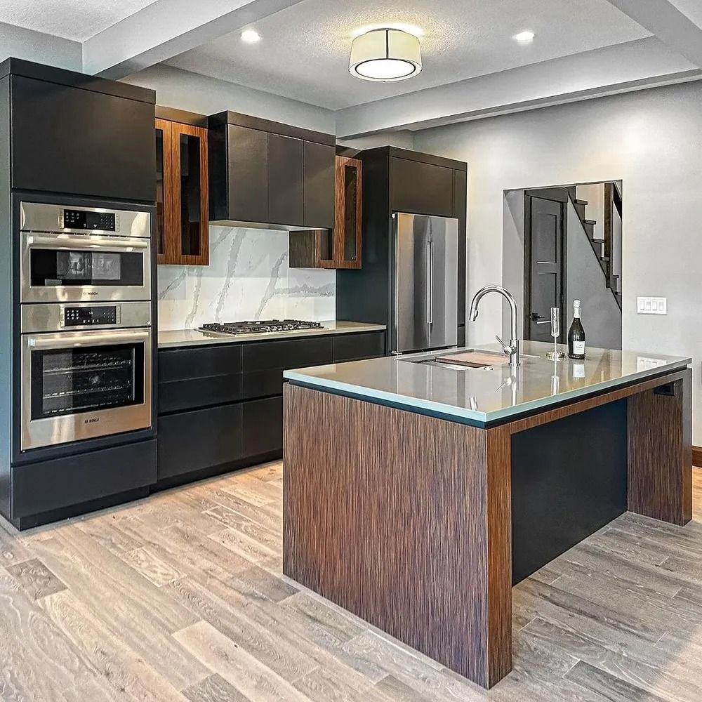 Modern kitchen with dark cabinetry, stainless steel appliances, and a wood island. Light wood floors and gray walls.
