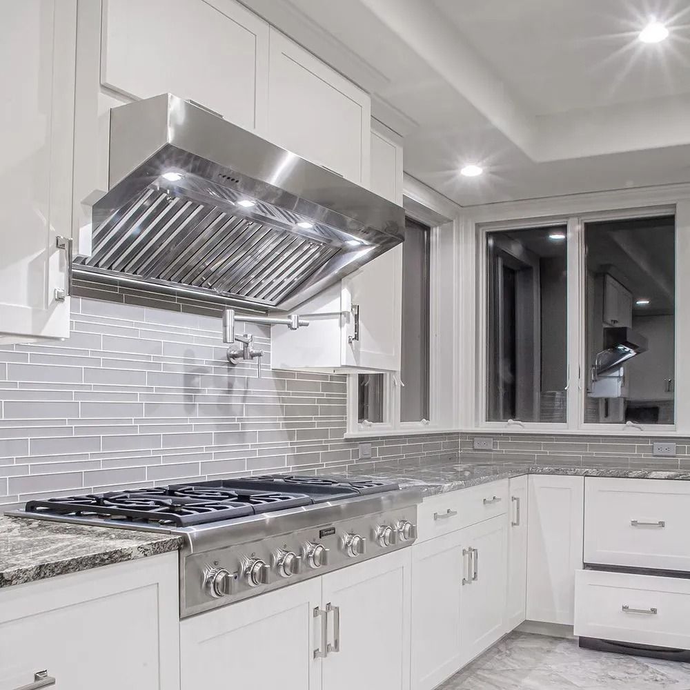 Modern white kitchen with stainless steel range hood, stove, and light grey backsplash.