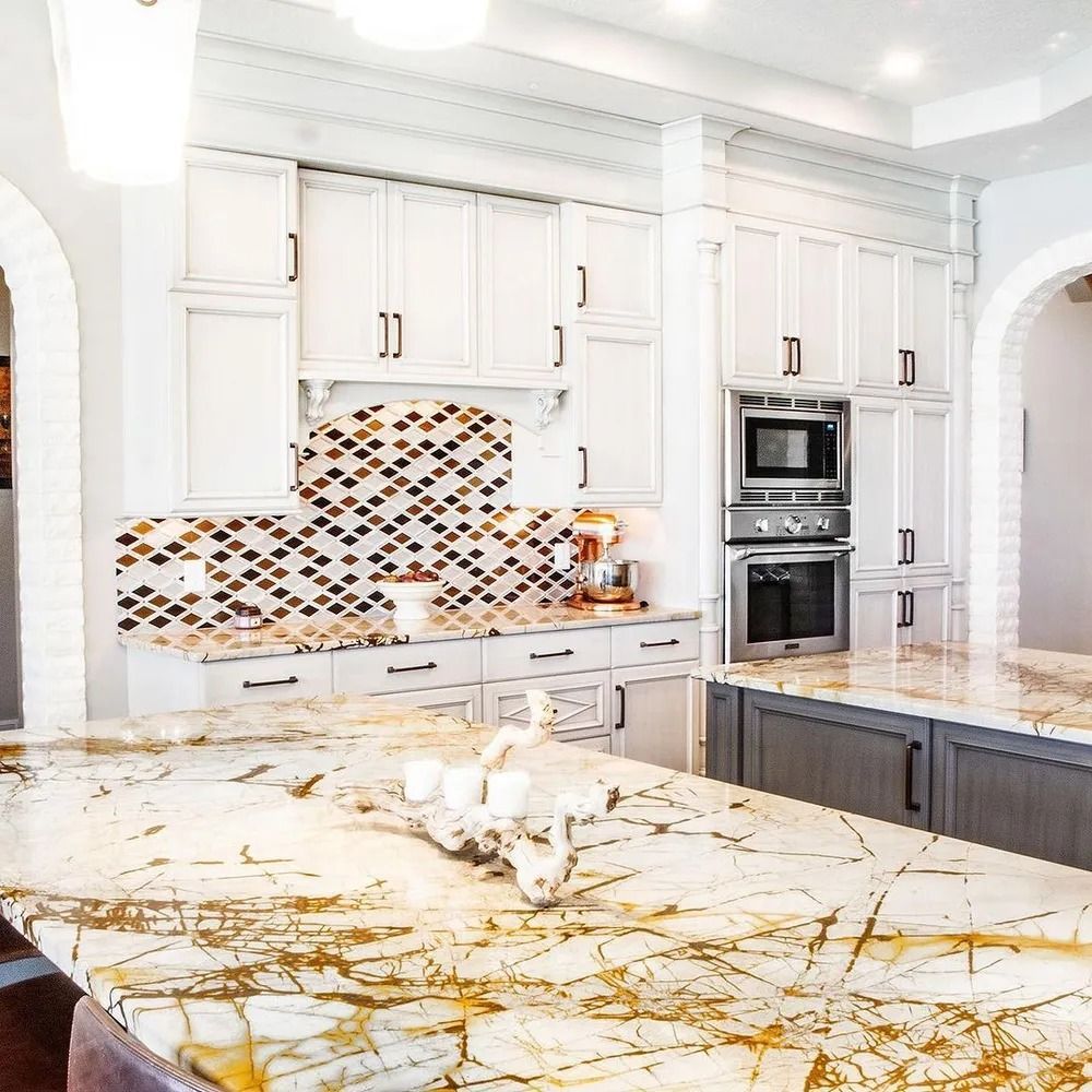 Elegant white kitchen with marble countertops, built-in appliances, and a mosaic backsplash.