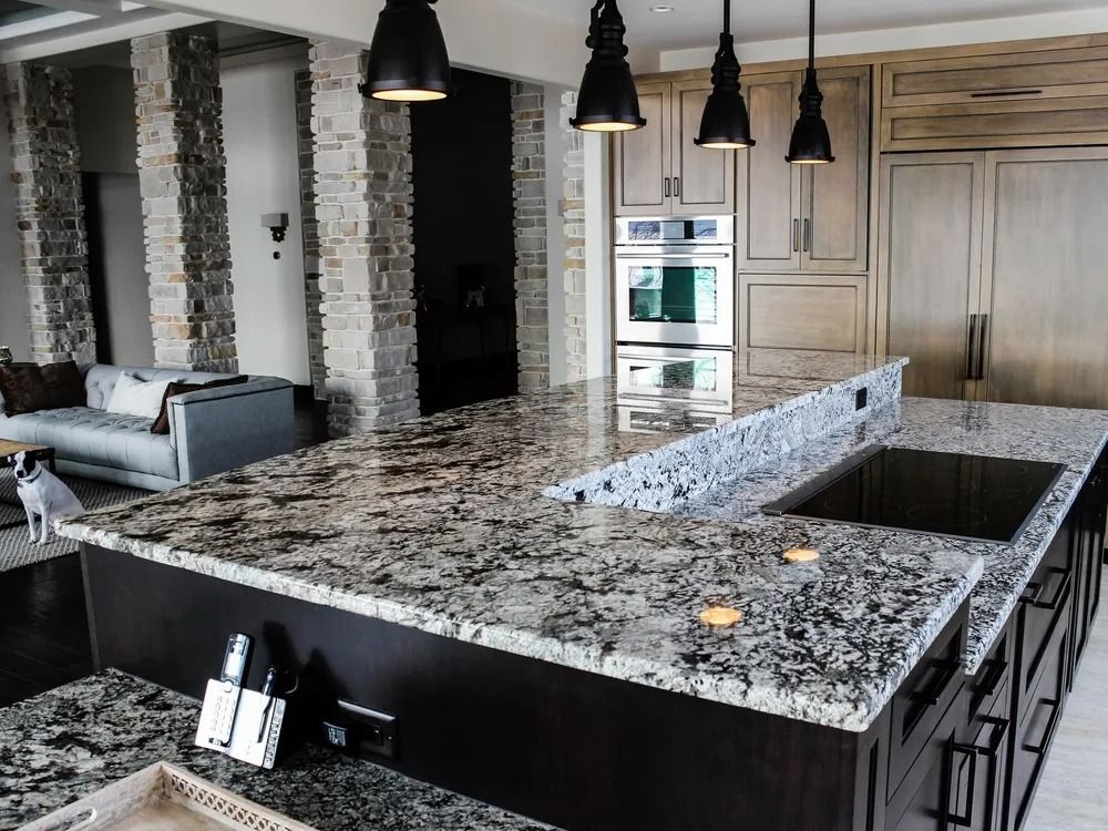 Modern kitchen with granite countertops, dark cabinets, and pendant lights.
