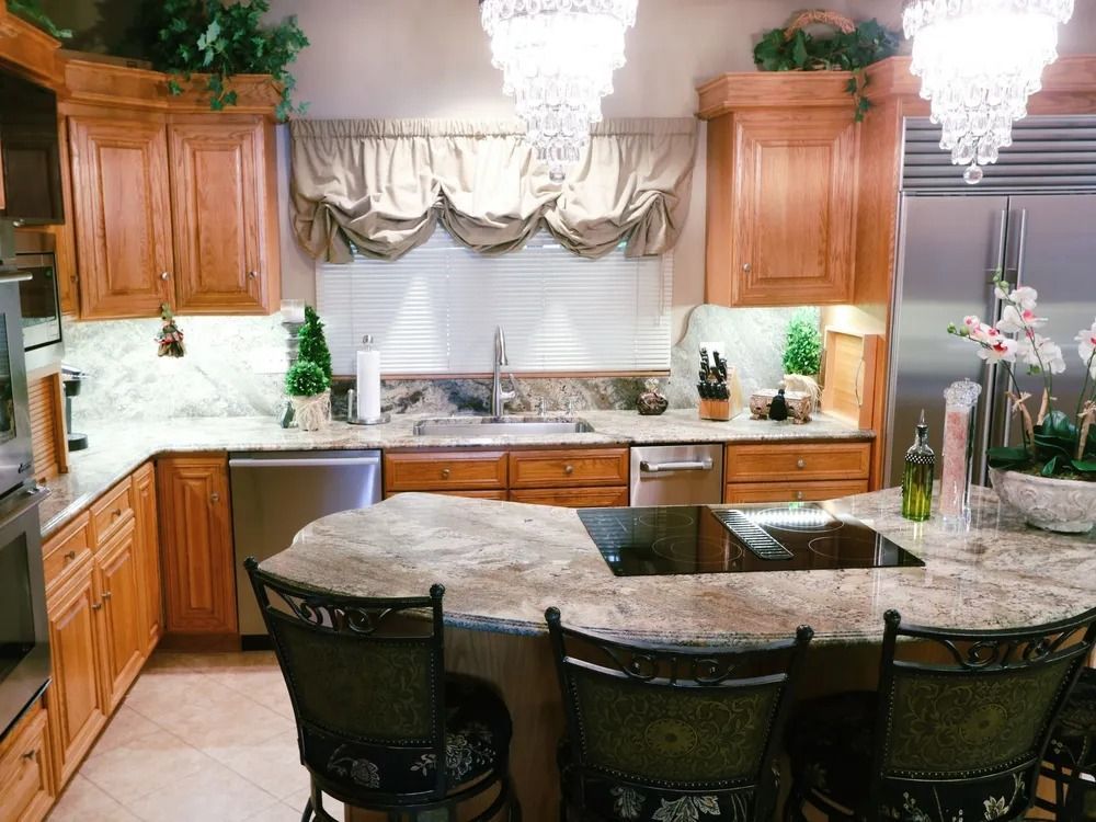 A kitchen with light wood cabinets, granite countertops, stainless steel appliances, and two crystal chandeliers.