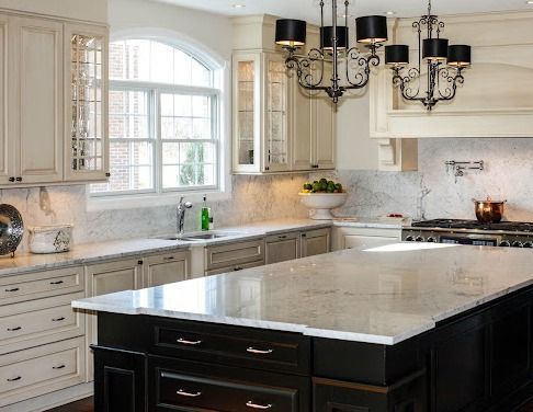 Kitchen with cream cabinets, dark island, granite countertops, and two chandeliers.