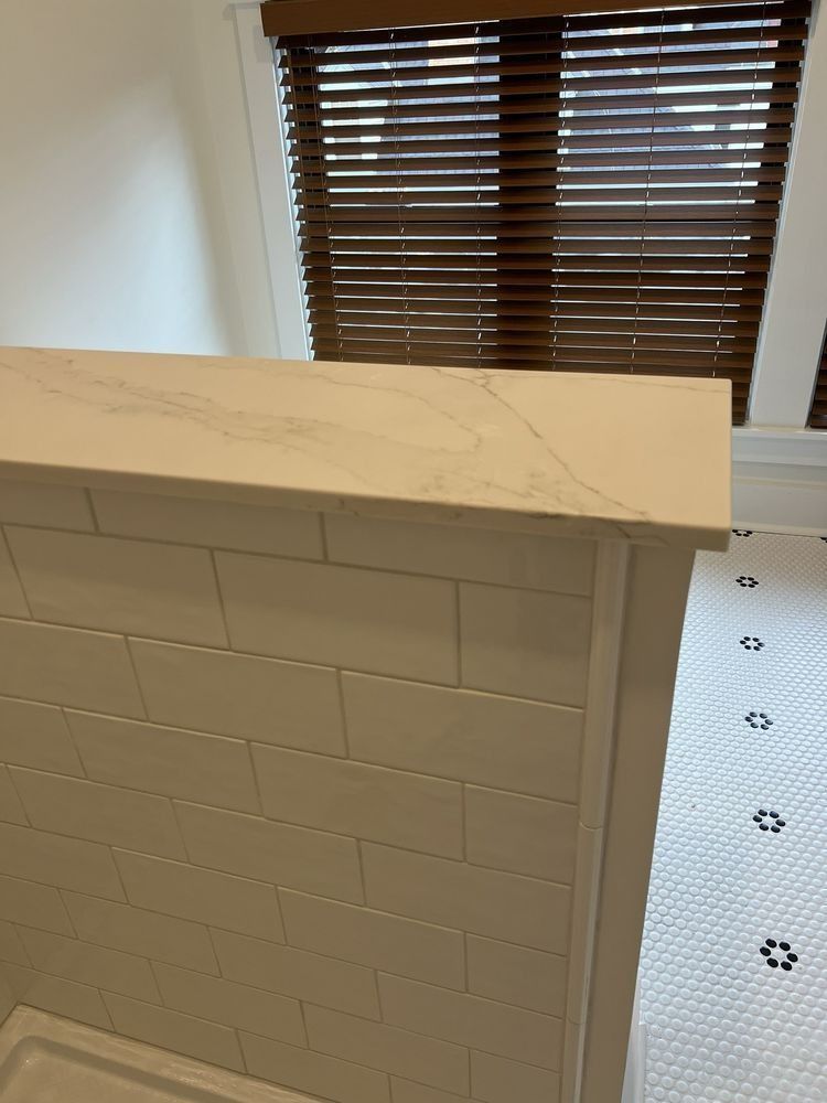 Cream-colored tiled wall with a light countertop. Brown blinds are in the background, set in a bathroom.