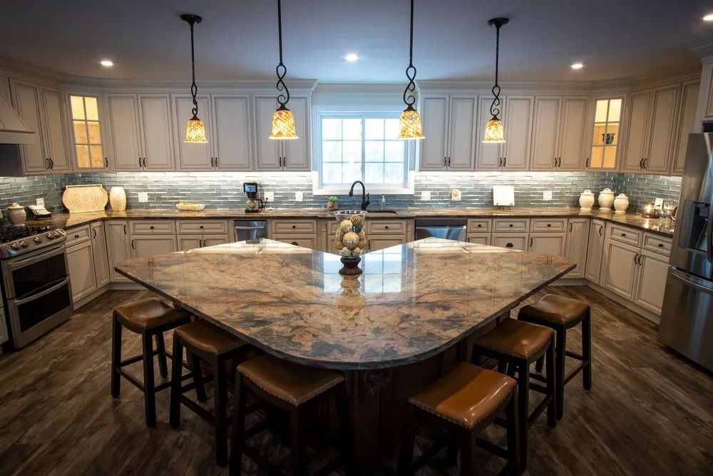 Kitchen with a large island and pendant lights. Light-colored cabinets, dark countertops, and wood flooring.